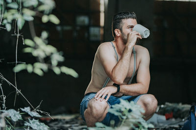 Full length of young man drinking glass sitting outdoors