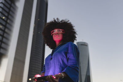 Red light falling on woman face wearing smart glasses in front of buildings