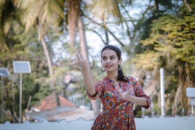 Portrait of young woman standing against trees