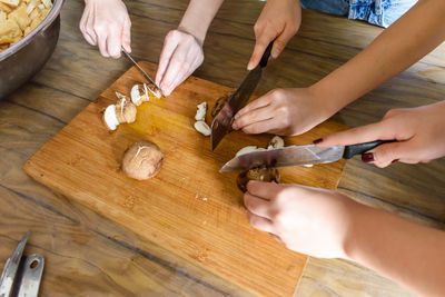 Cropped hands of people chopping mushrooms on table