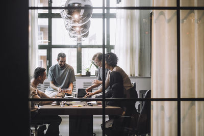 Smiling businessmen and businesswomen discussing in meeting room seen through glass