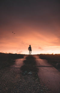 Silhouette man standing on road against sky during sunset