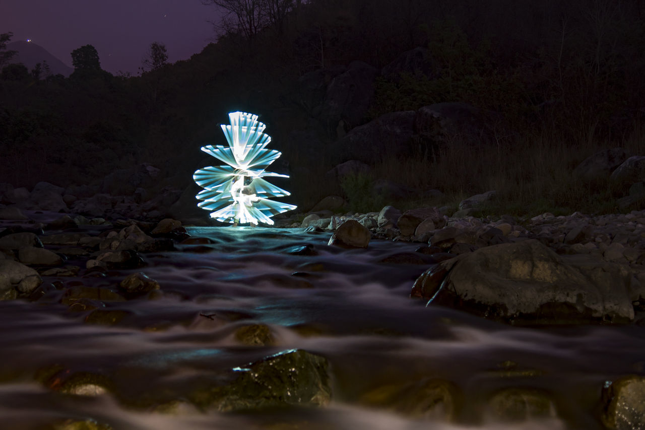 ILLUMINATED LIGHT PAINTING ON ROCK BY RIVER AGAINST SKY