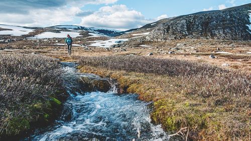 Woman walking by stream on land during winter