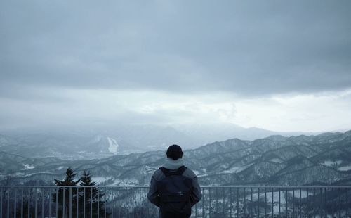 Person standing by railing at observation point against mountain range