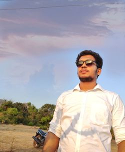 Young man wearing sunglasses standing against sky