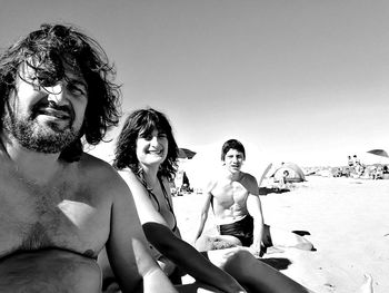 Portrait of friends sitting at beach during sunny day