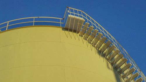 Low angle view of yellow oil storage tank against clear blue sky
