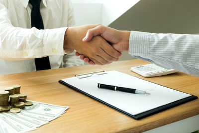Midsection of real estate agent and client shaking hands on table