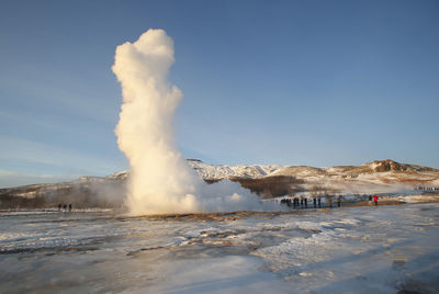 People watching geyser on snow covered landscape against sky
