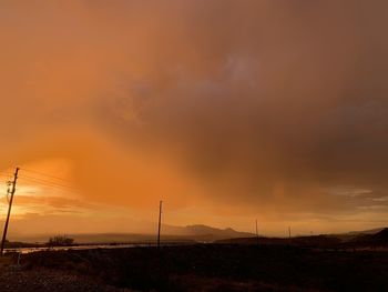 Silhouette electricity pylon on field against dramatic sky during sunset