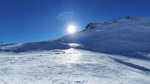 Scenic view of snow covered mountains against bright sun