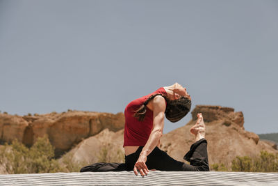 Low angle view of woman exercising while sitting on car roof against clear sky