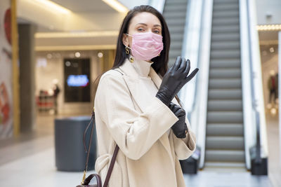 Portrait of woman wearing mask standing against escalator