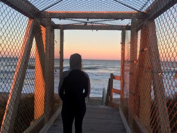 Rear view of person standing on pier by sea during sunset