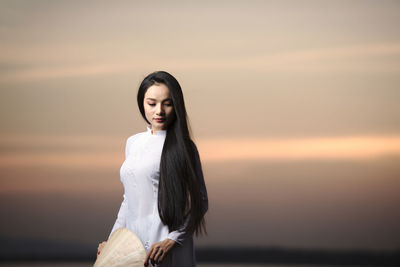 Young woman standing by sea against sky during sunset