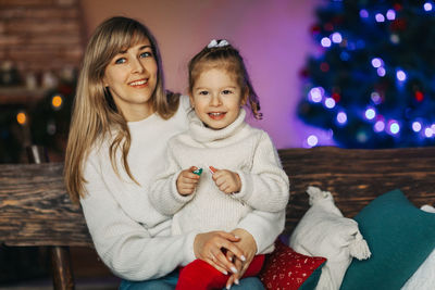 Portrait of a happy little girl sitting on her mother's lap and drinking hot chocolate on christmas