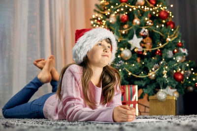 Happy new year and happy christmas. a cute girl in a santa hat lies next to beautiful christmas tree