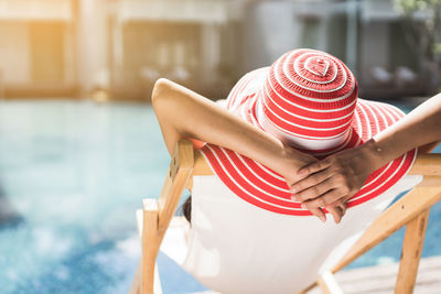 Rear view of woman wearing hat while relaxing on deck chair at poolside during sunny day