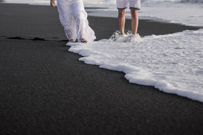 Low section of couple standing on shore at beach