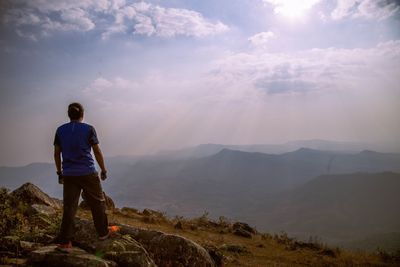 Rear view of man standing on rock against sky