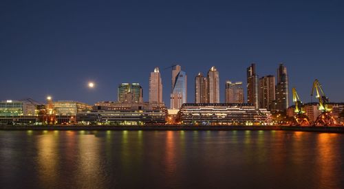 River by illuminated cityscape against sky at dusk