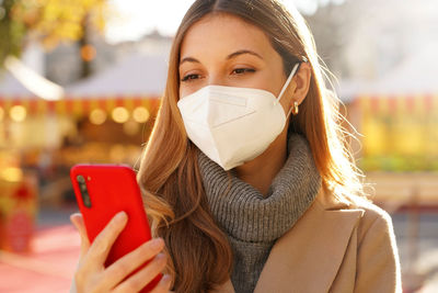 Close up of beautiful girl with medical mask ffp2 kn95 watching her smartphone in christmas markets