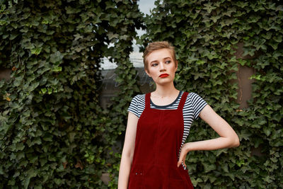 Portrait of beautiful young woman standing against plants