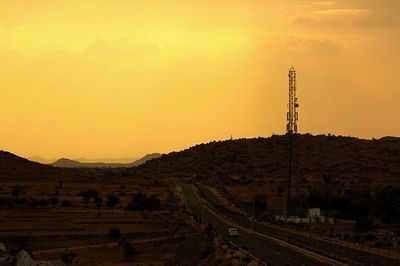 Electricity pylon by road against sky during sunset