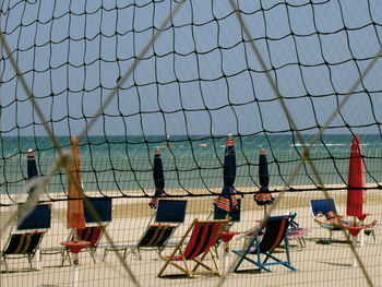 Beach chairs by sea seen through volleyball net