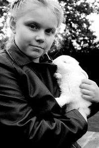 Portrait of cute girl holding rabbit while standing outdoors