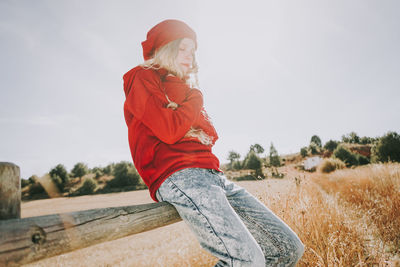 Side view of woman sitting on railing against clear sky during sunny day