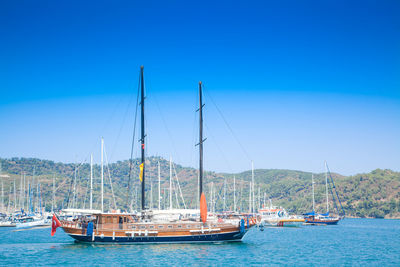 Sailboats moored in sea against clear blue sky