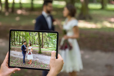 A pre-ceremony photo session of dressed wedding couple in a nature park and on a screen of a tablet