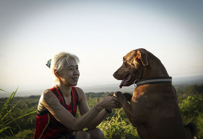 Portrait of young woman with dog sitting on field