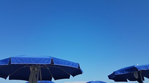 Low angle view of parasols against clear blue sky