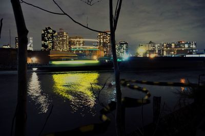 Illuminated city by river against sky at night