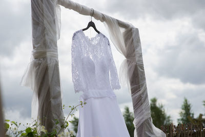 Low angle view of bride dress hanging on wood against cloudy sky