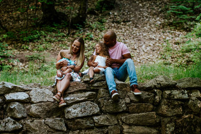 Happy young diverse family sitting on rocks in forest smiling