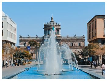 Fountain in swimming pool against buildings in city