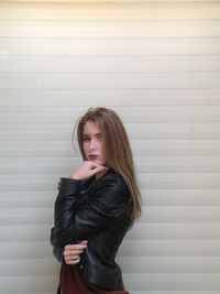 Portrait of young woman standing with hand on chin against wall