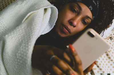 Young woman using mobile phone while lying on bed at home