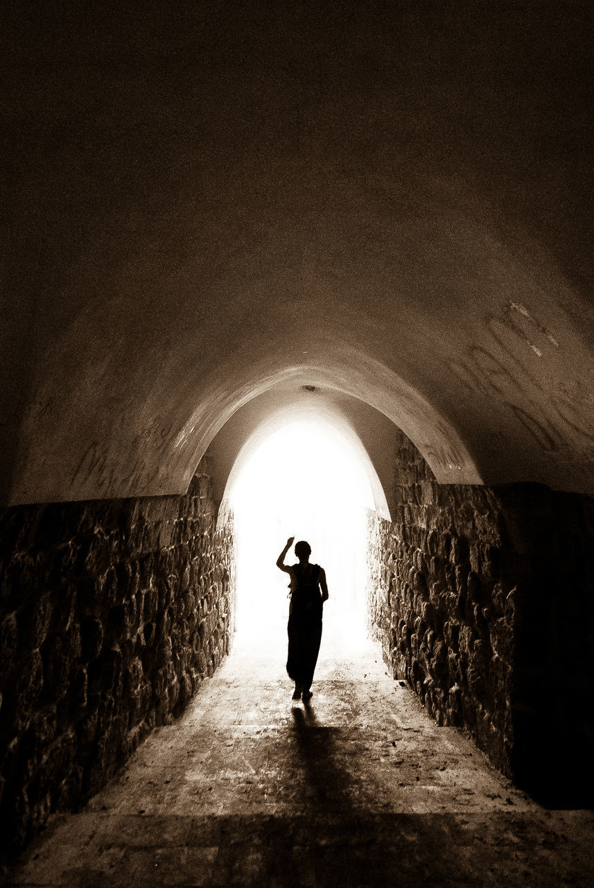 architecture, arch, one person, tunnel, built structure, standing, full length, real people, silhouette, the way forward, direction, lifestyles, leisure activity, rear view, day, men, walking, indoors, wall, light at the end of the tunnel, stone wall, arched