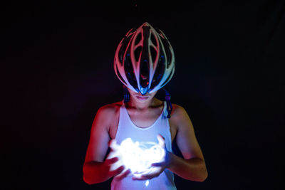 Midsection of woman holding illuminated lighting equipment against black background