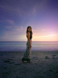 Woman standing at beach against sky during sunset