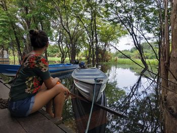 Woman sitting by lake against trees