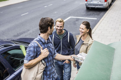 Happy friends with man putting newspaper in recycling bin