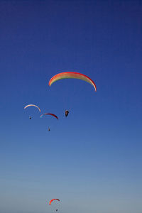 Low angle view of people paragliding against clear blue sky