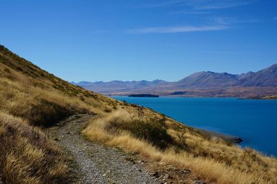 Scenic view of landscape and mountains against blue sky with a hiking path.