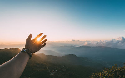 Copped hand of person against sky during sunset